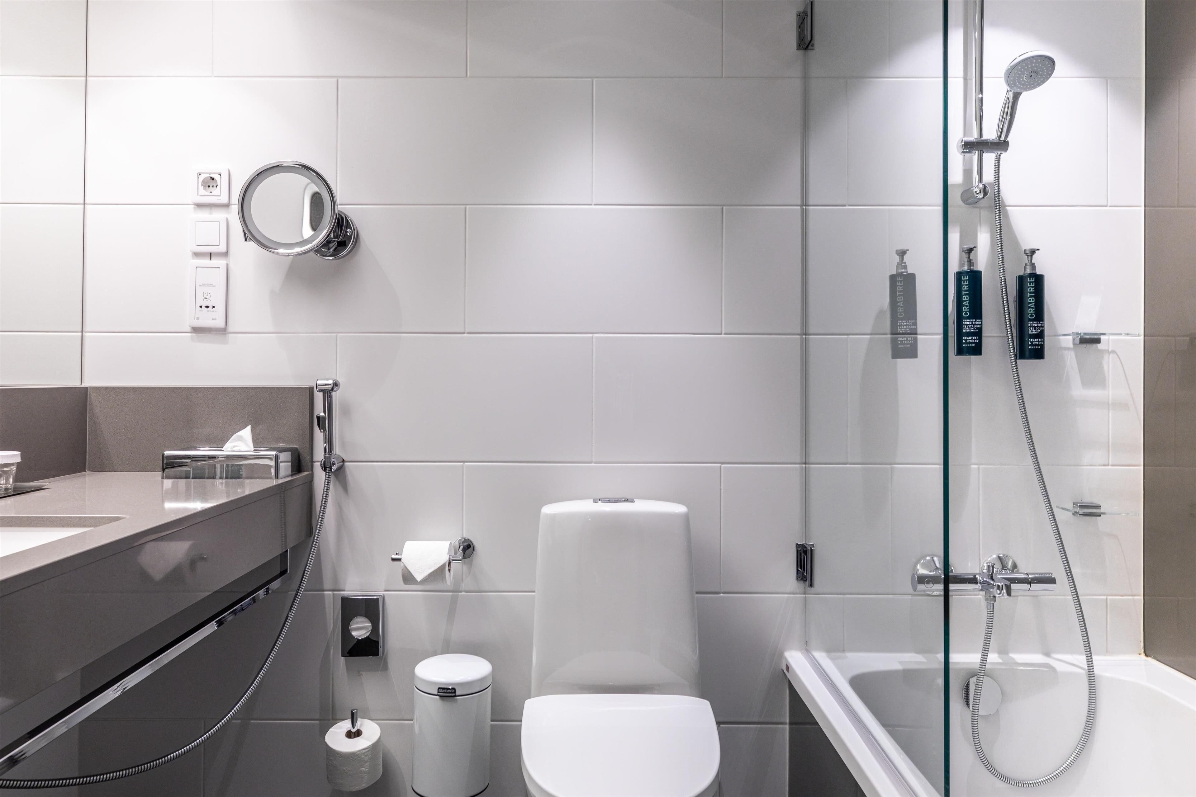 Een moderne badkamer met een douche met glazen wand, toilet, bidet en een wastafel met spiegel.