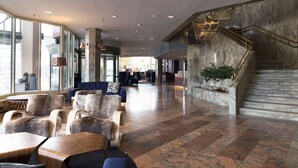 Eine großzügige Lobby mit einer Marmortreppe, Sitzbereichen und großen Fenstern.