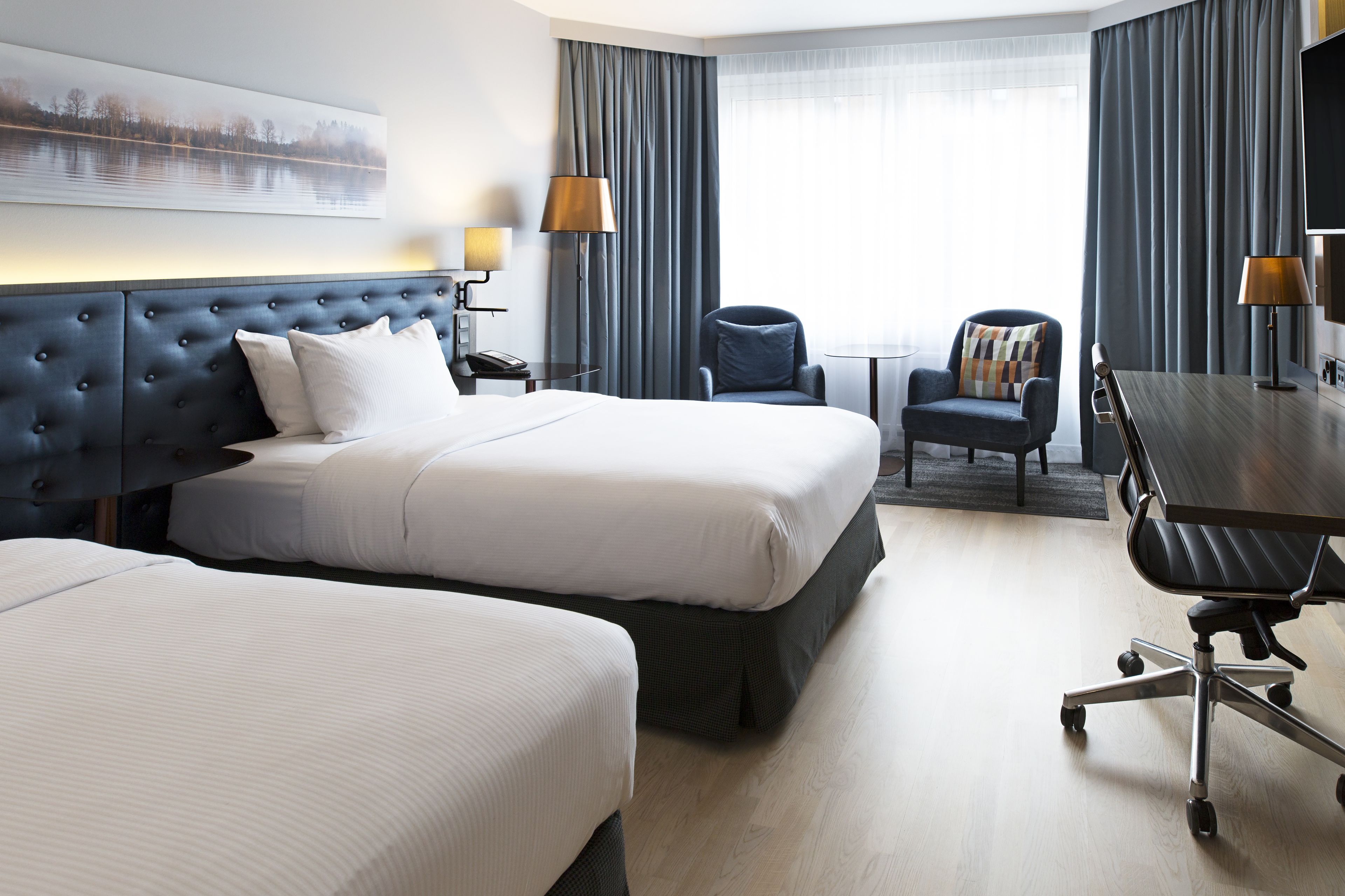 Habitación de hotel con dos camas, un escritorio, una silla y un televisor.