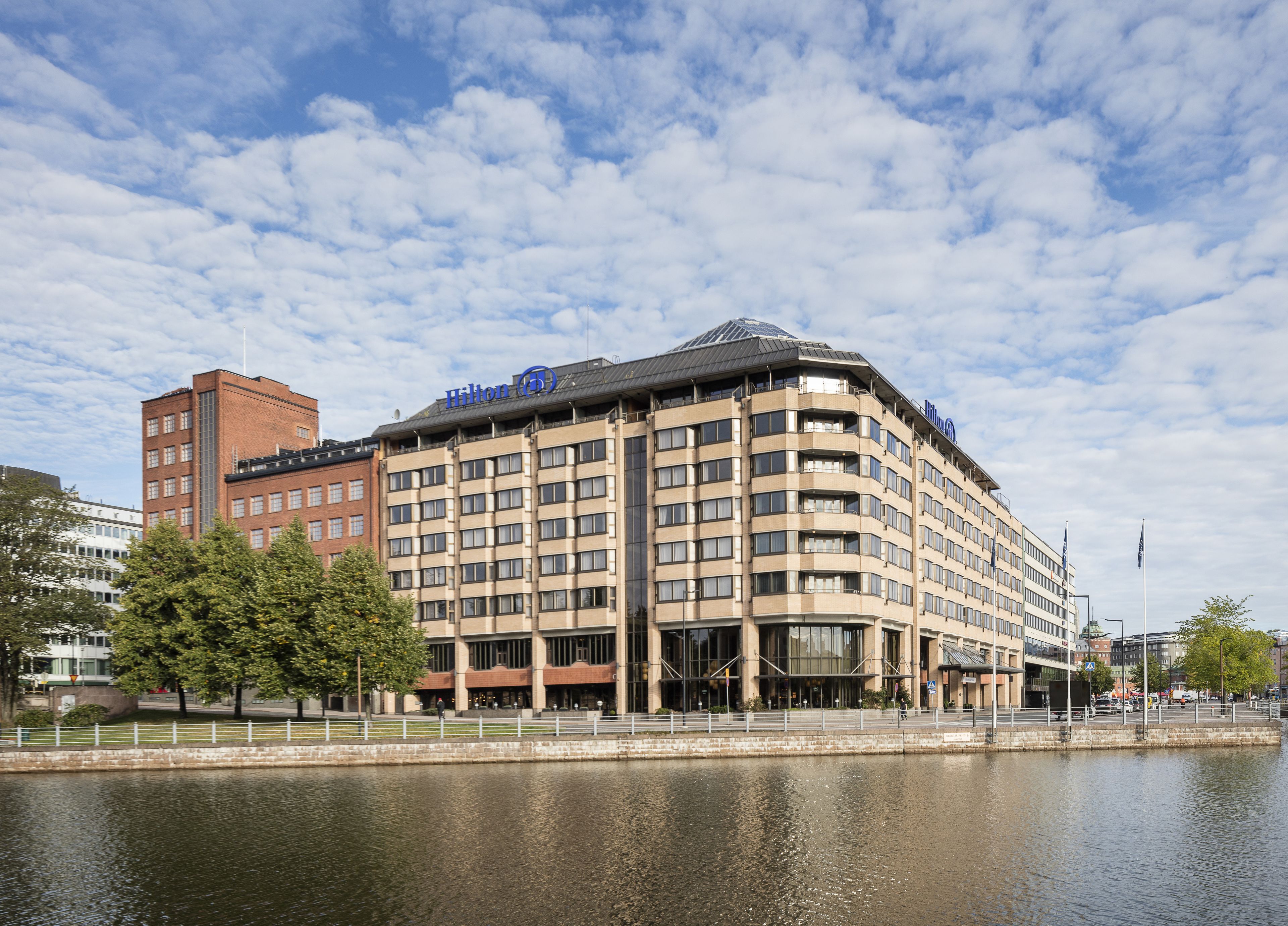 A multi-story hotel with a prominent Hilton logo, situated beside a body of water.