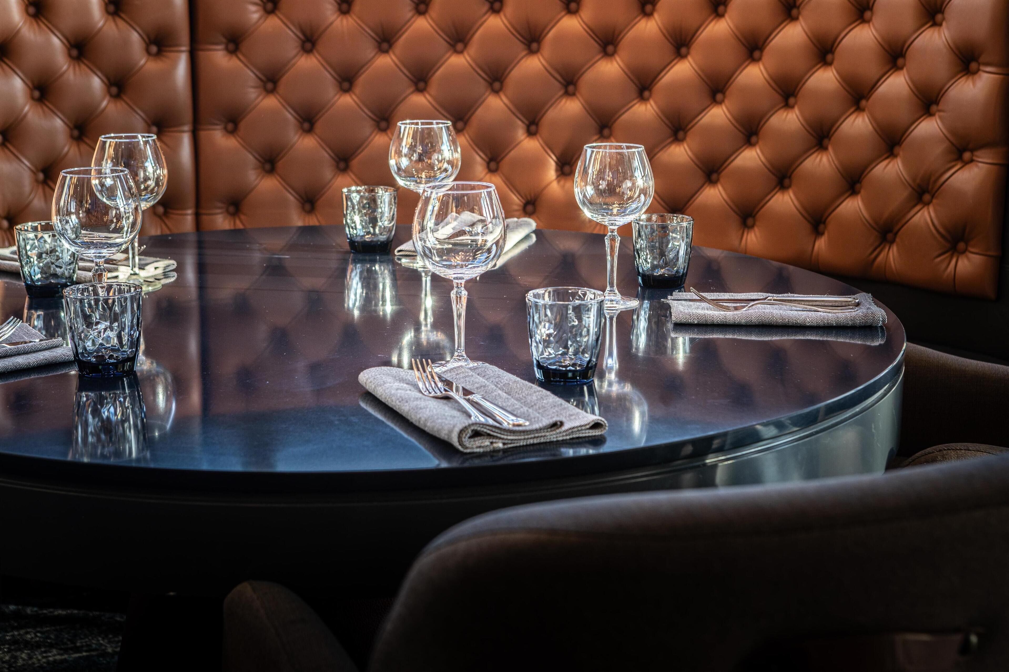 A round dining table with a dark reflective surface, surrounded by brown upholstered chairs.