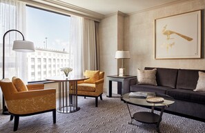 Una habitación de hotel moderna con sofá, sillones, una mesa de centro y un ventanal con vistas a la ciudad.