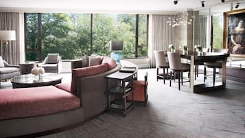 Un salon moderne comprenant un canapé, des fauteuils, une table à manger et une grande fenêtre donnant sur un paysage arboré.