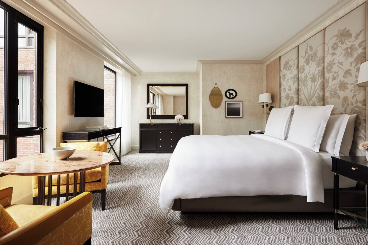 Ein Hotelzimmer mit einem großen Bett, einem Fernseher, einem Schreibtisch und einem Essbereich.
