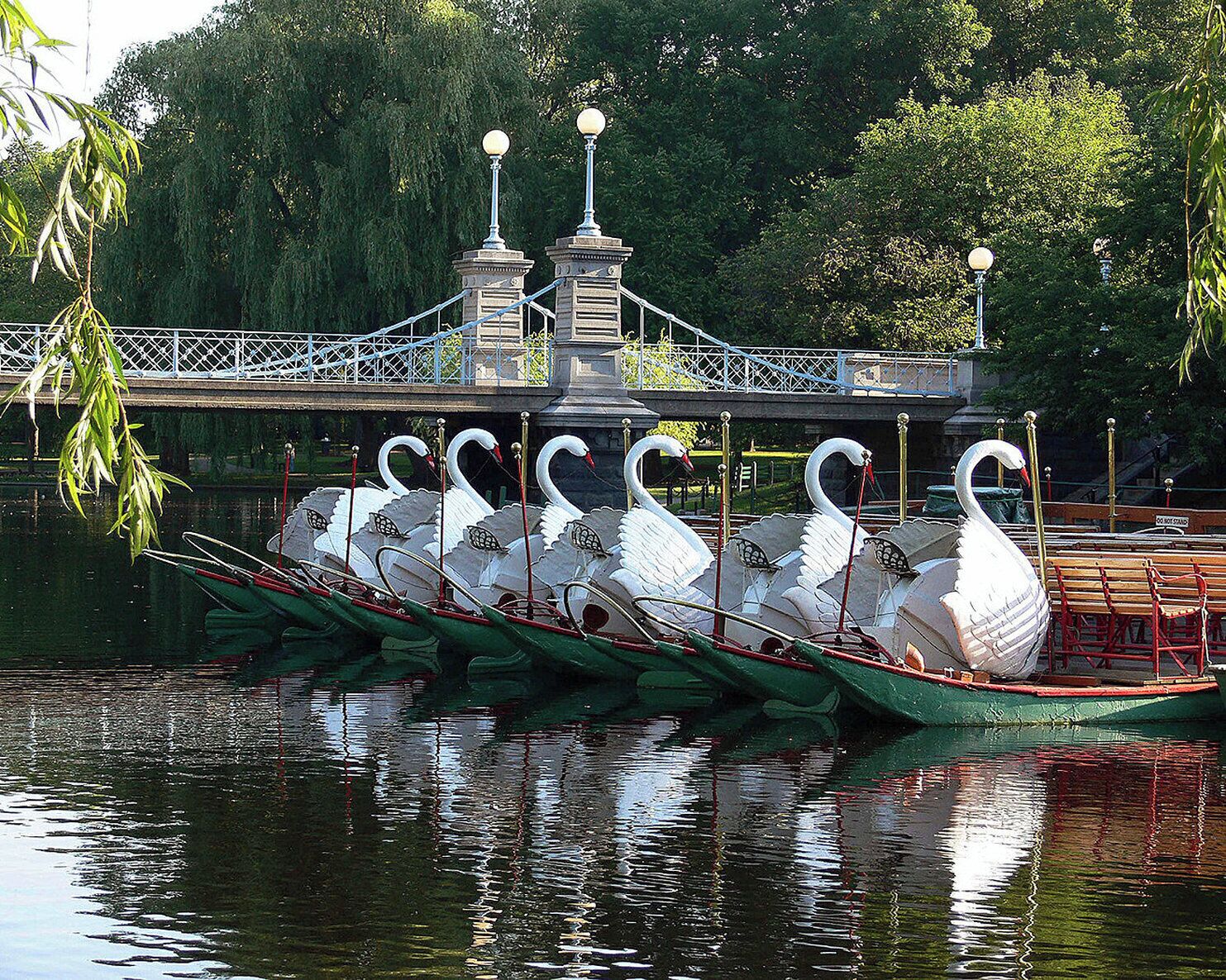 A rowboat with swan-shaped seats and a bridge in the background.