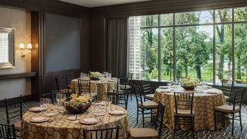 A dining area with round tables, black chairs, and a view of trees through large windows.
