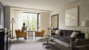 Una sala de estar moderna con un sofá, sillones, una mesa de centro de vidrio y un ventanal con vistas a árboles.