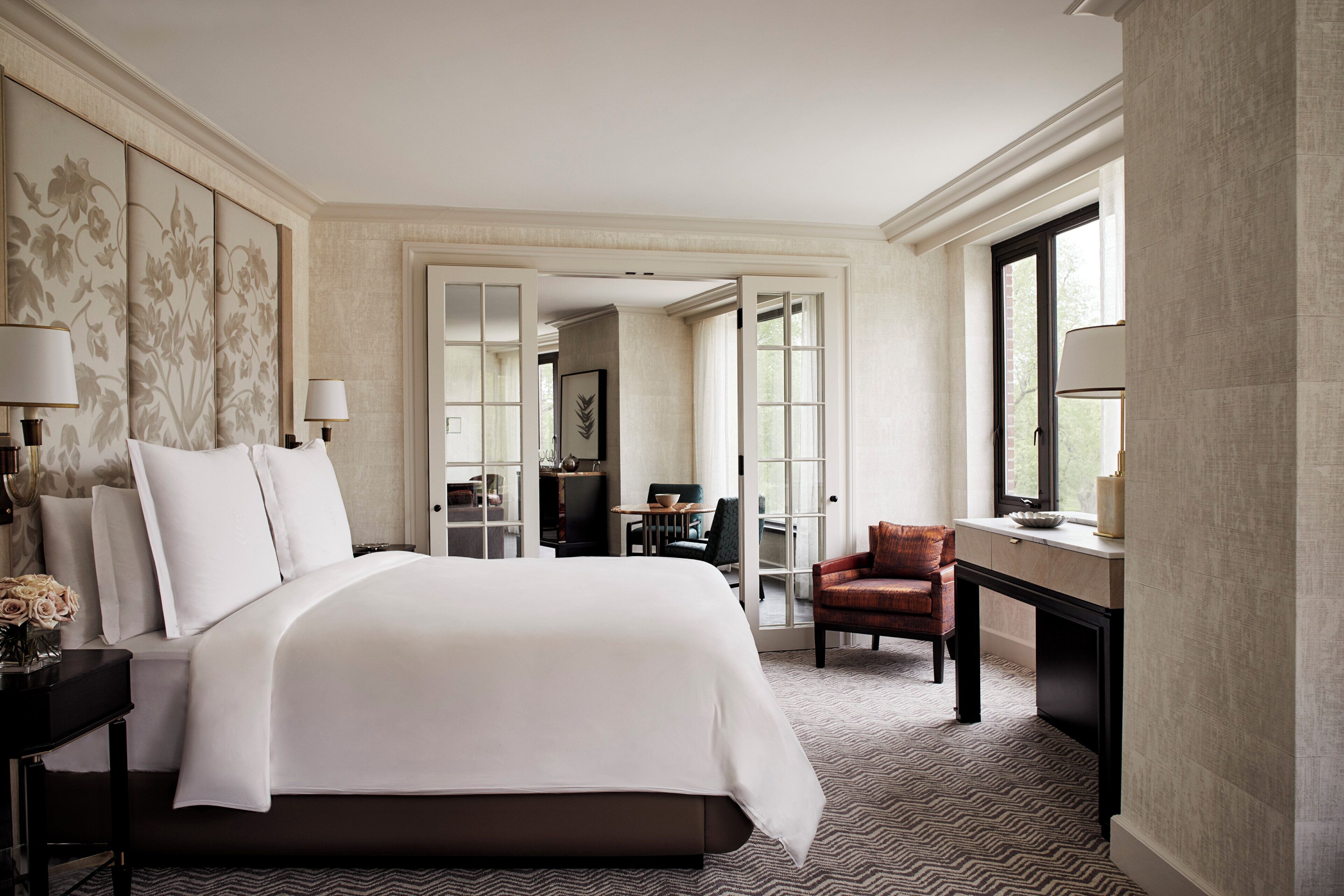 A hotel room with a large bed, a desk, a chair, and a view of the outdoors through a window.