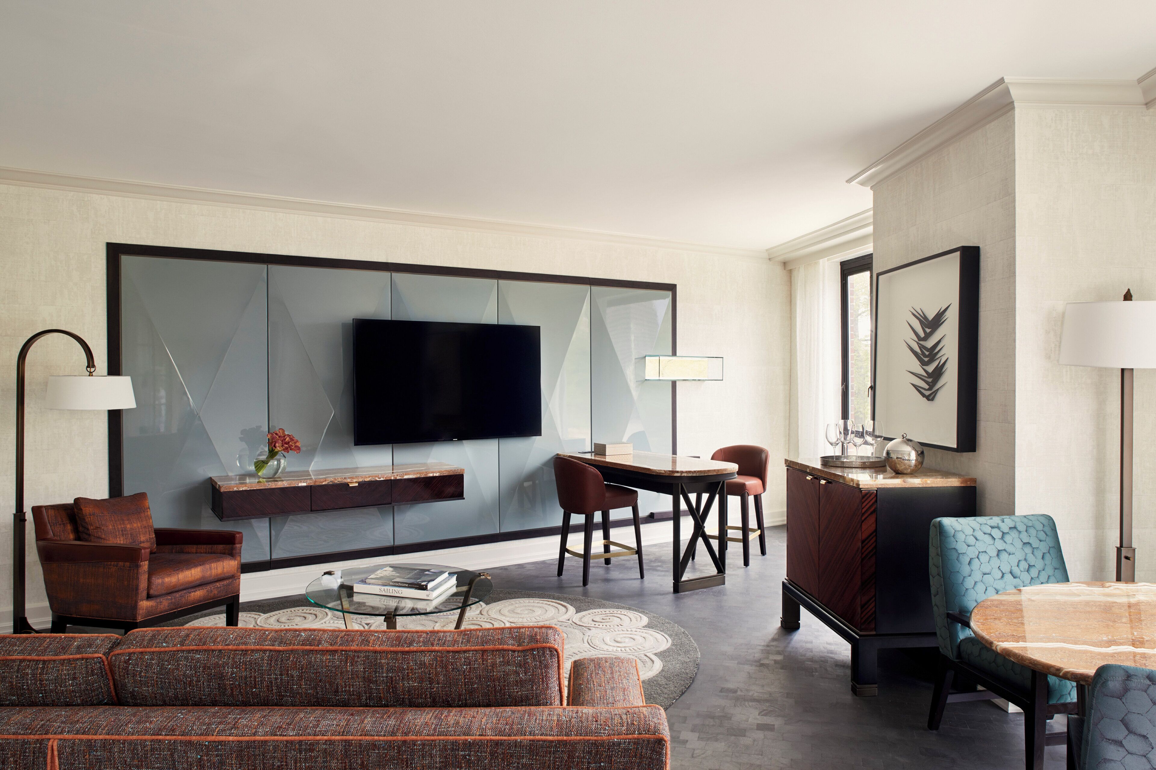 A modern living room with a flat-screen TV, comfortable seating, a dining area, and a large window.
