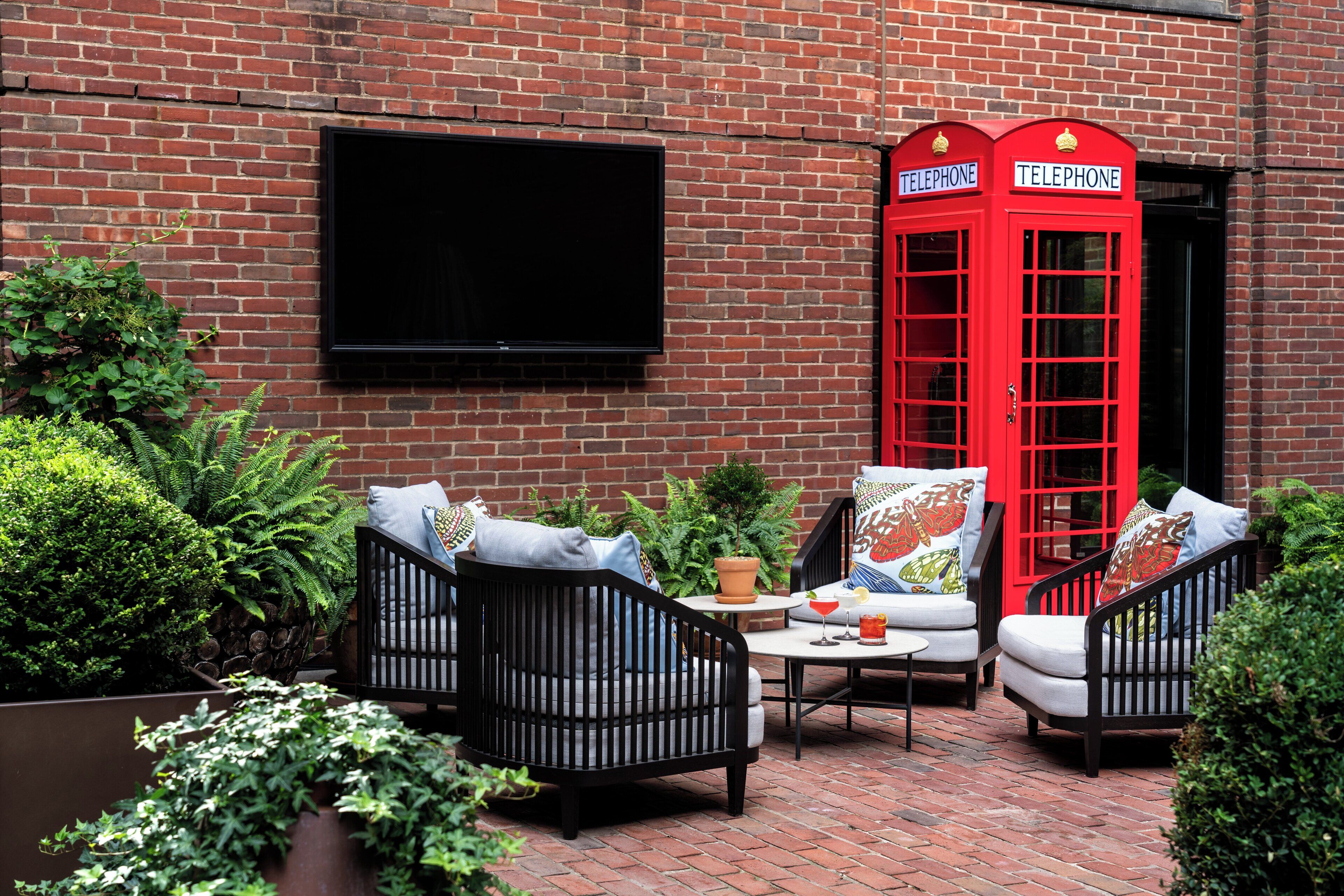 A brick wall with a red telephone booth and a flat-screen TV mounted on it.