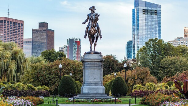 A statue in a park with a cityscape in the background.
