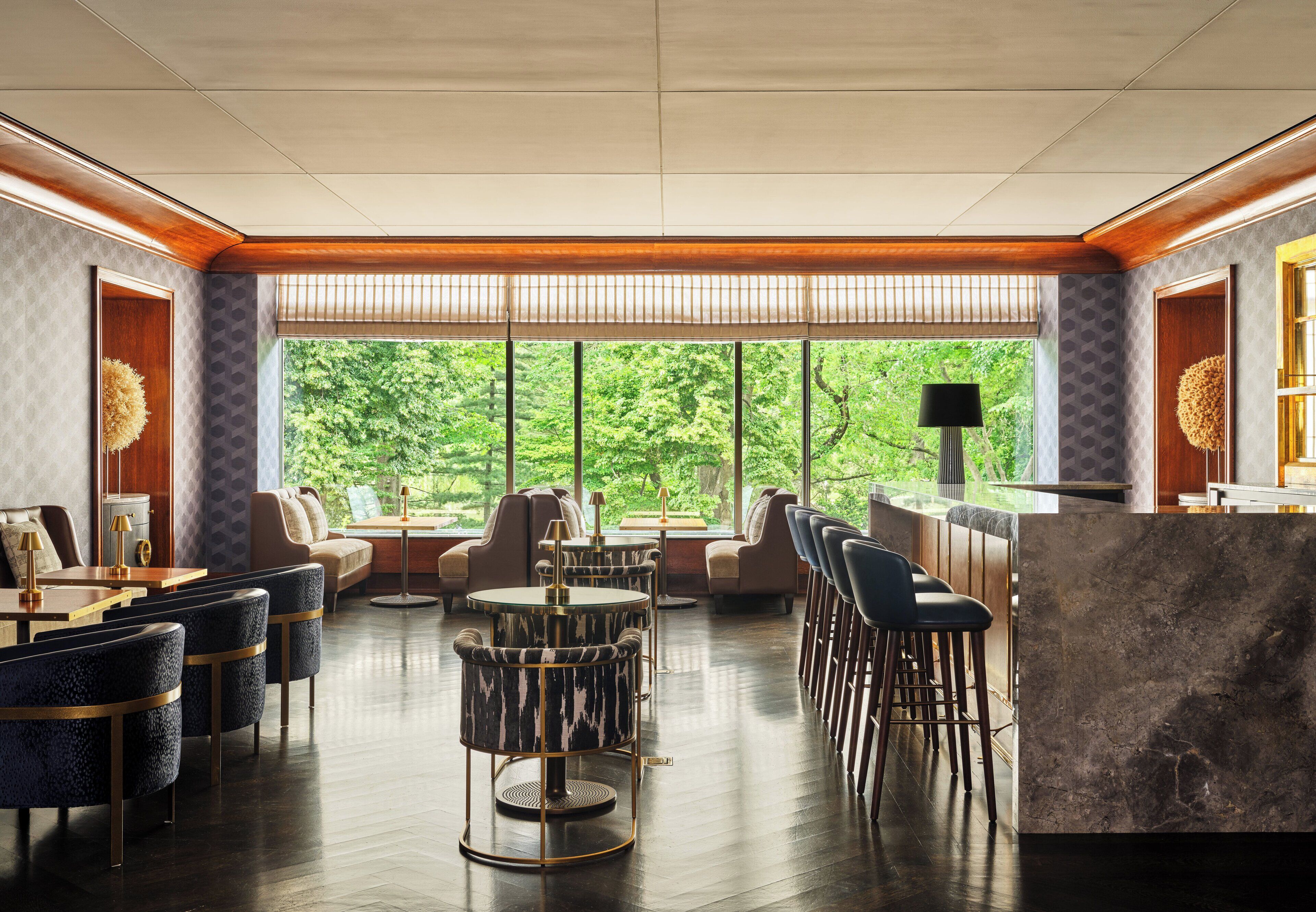 A modern lounge with a bar area, seating arrangements, and large windows offering a view of greenery.
