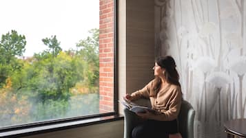 A person sitting by a window with a view of trees, reading a book.