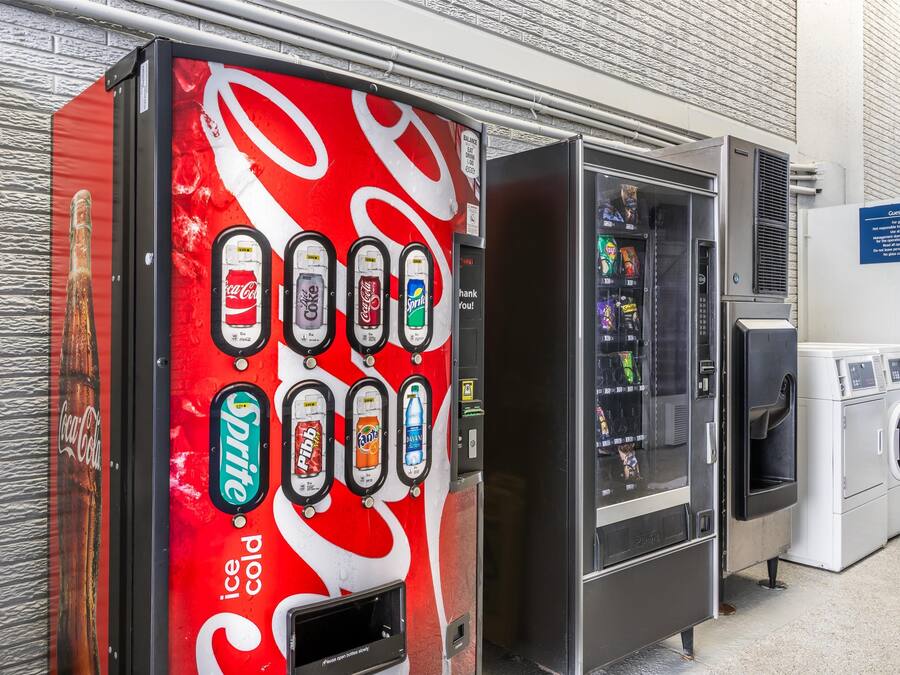 En automat med forskellige drikkevarer og et område med vaskemaskiner og tørretumblere for gæster.