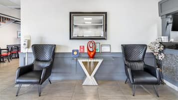 Una zona de recepción con dos sillones de cuero negro, una mesa de vidrio y un certificado enmarcado en la pared.