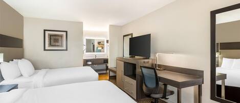 Una habitación de hotel con dos camas, un escritorio, una silla, un televisor y un espejo.