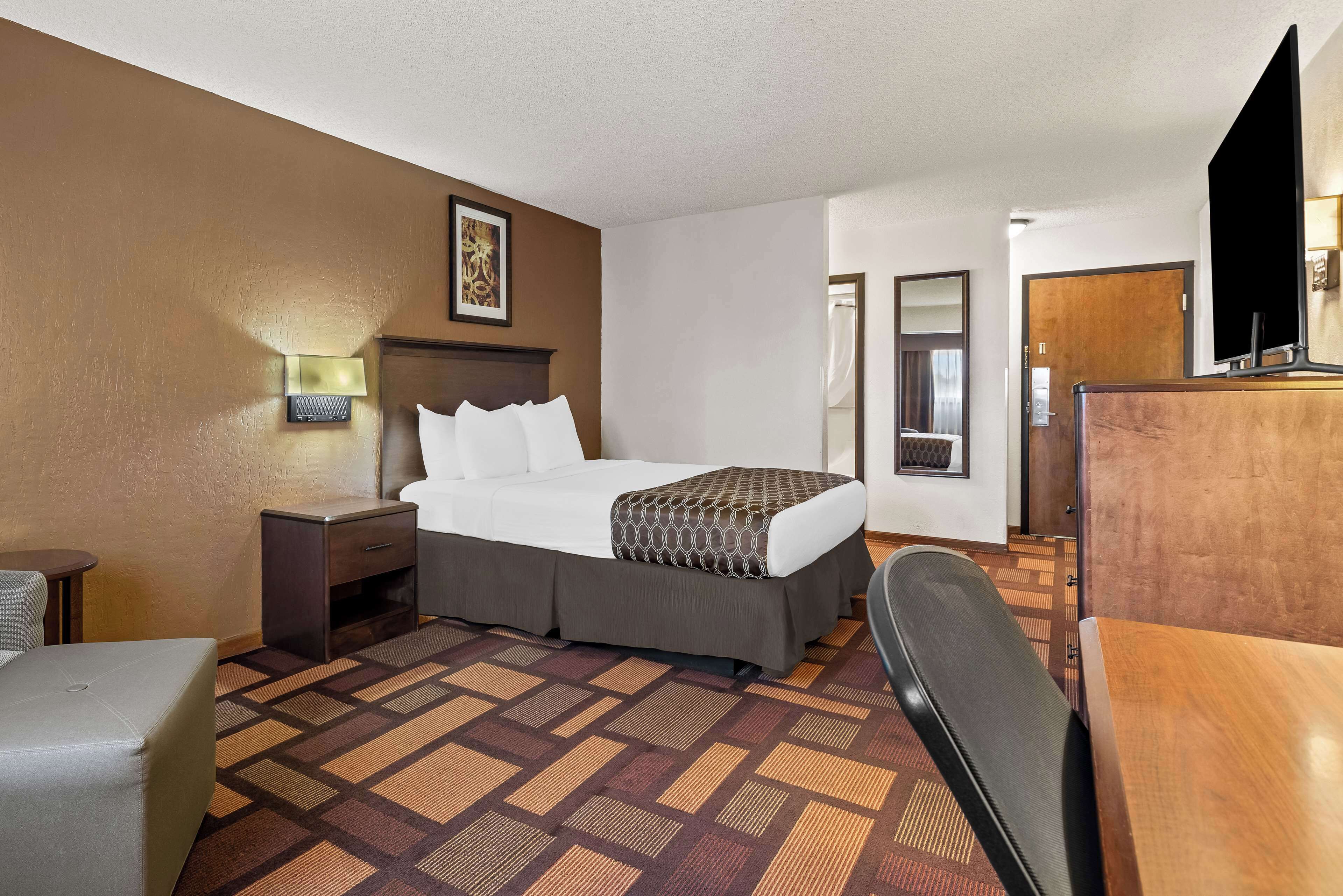 A hotel room with a bed, bedside table, lamp, and a desk with a chair.