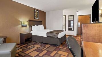 A hotel room with a bed, bedside table, lamp, and a desk with a chair.