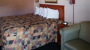 A hotel room with a bed, a chair, two bedside lamps, a painting on the wall, and a telephone on the nightstand. - Rodeway Inn Leesburg Chain of Lakes (Leesburg)
