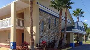 A two-story building with a stone facade, a balcony on the ground floor, and palm trees in the foreground. - Rodeway Inn Leesburg Chain of Lakes (Leesburg)