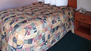 A neatly made bed with a patterned quilt, a wooden headboard, two bedside lamps, a bedside telephone, and a small wooden nightstand. - Rodeway Inn Leesburg Chain of Lakes (Leesburg)