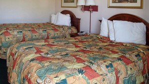 A hotel room with two beds, each with a floral-patterned bedspread, a nightstand with a lamp, and two framed pictures on the wall. - Rodeway Inn Leesburg Chain of Lakes (Leesburg)