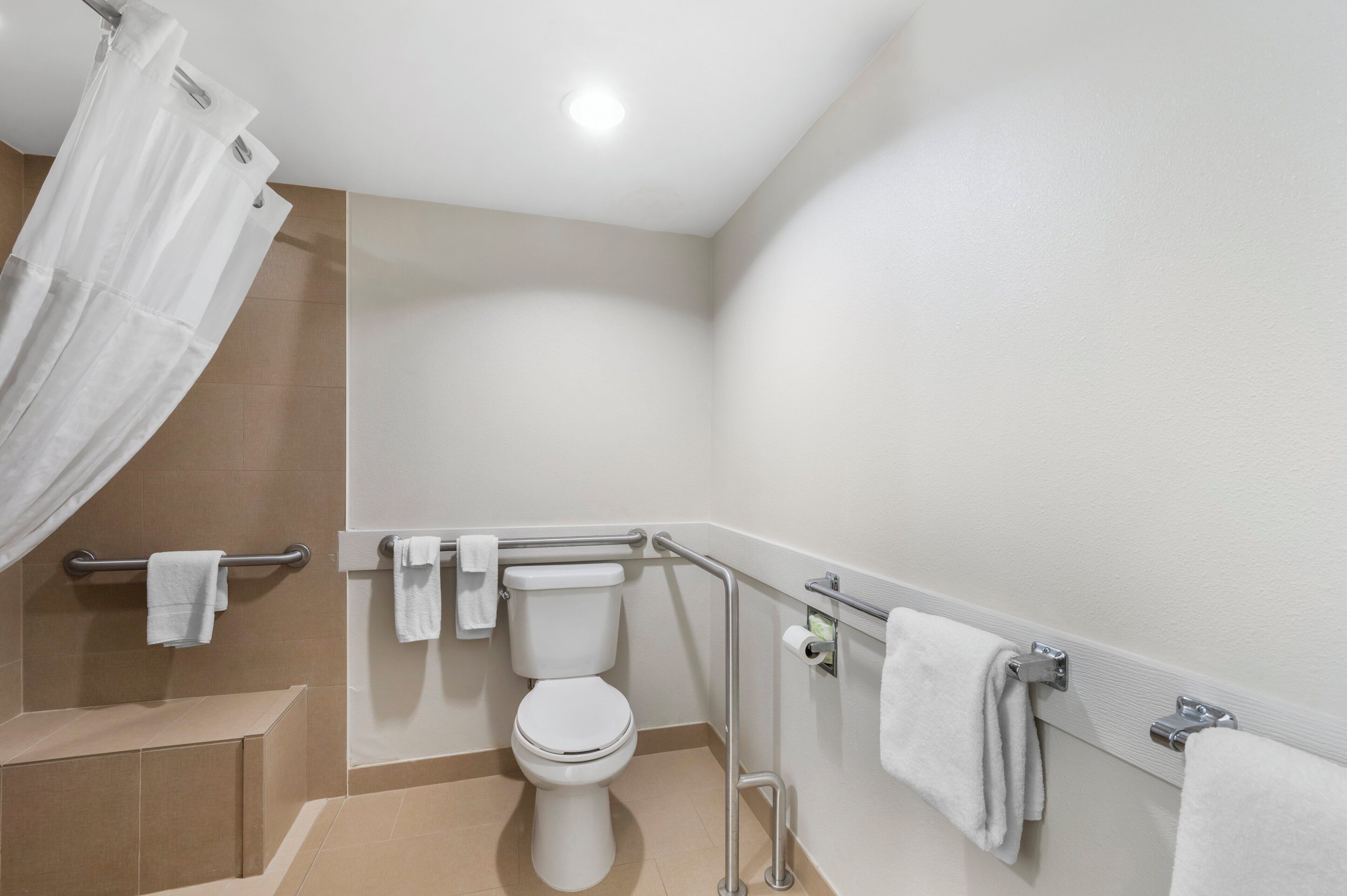 A bathroom with a toilet, grab bars, a shower curtain, and a towel rack.