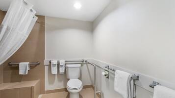 A bathroom with a toilet, grab bars, a shower curtain, and a towel rack.