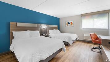 A hotel room with two beds, a desk, a chair, a window, and a wall art piece.