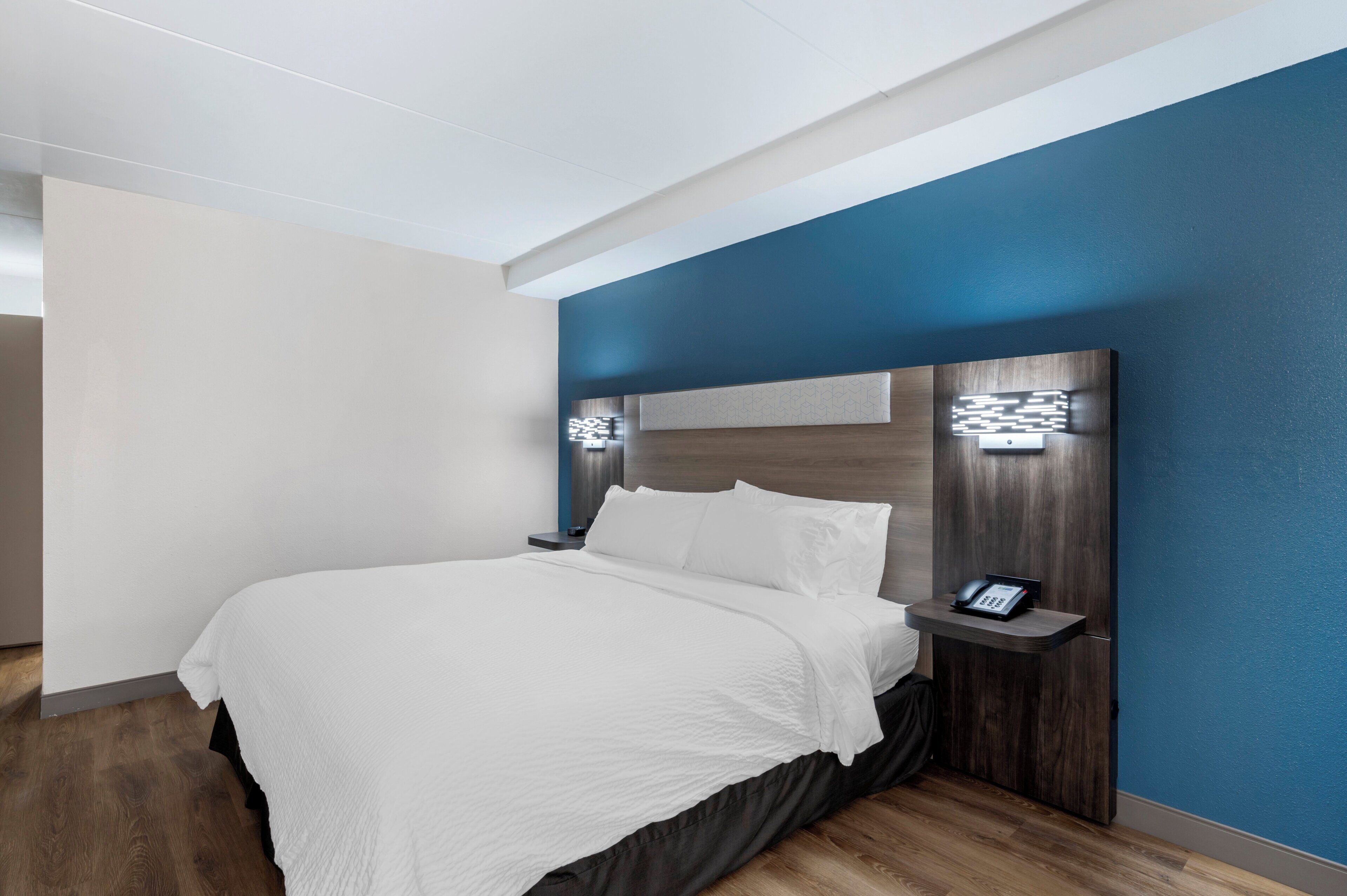 Une chambre d’hôtel équipée d’un lit, d’une table de chevet, d’un téléphone et d’un luminaire fixé au mur.