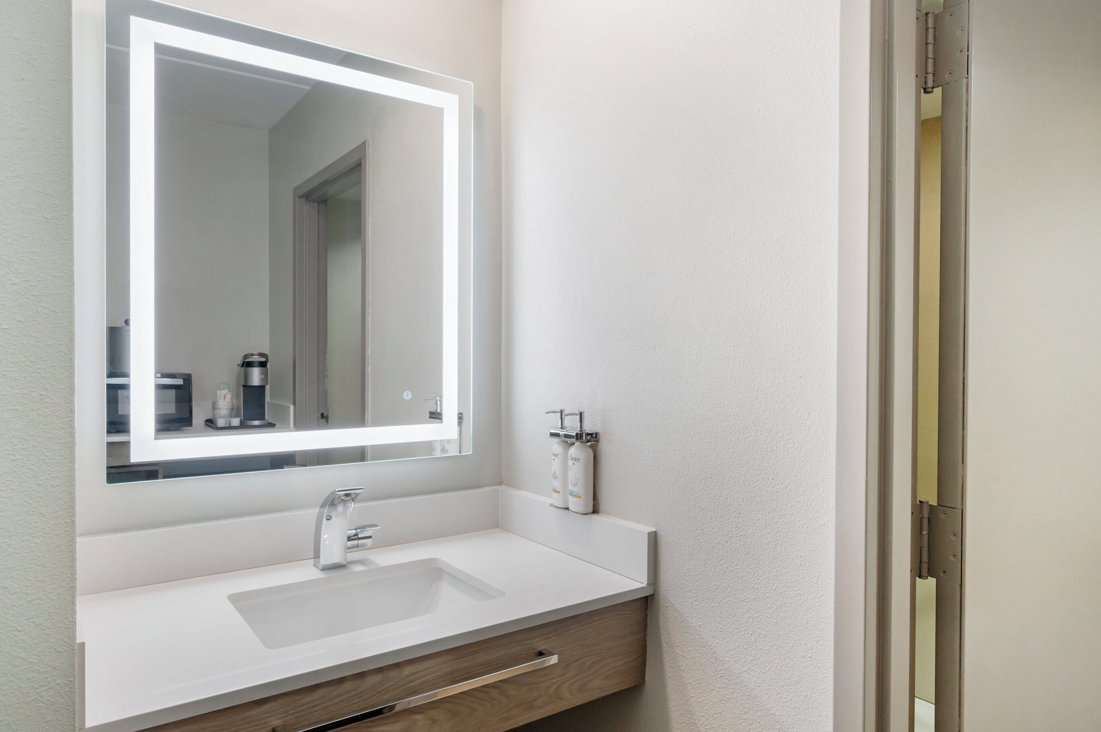 A bathroom with a white sink, a mirror, and a towel dispenser.