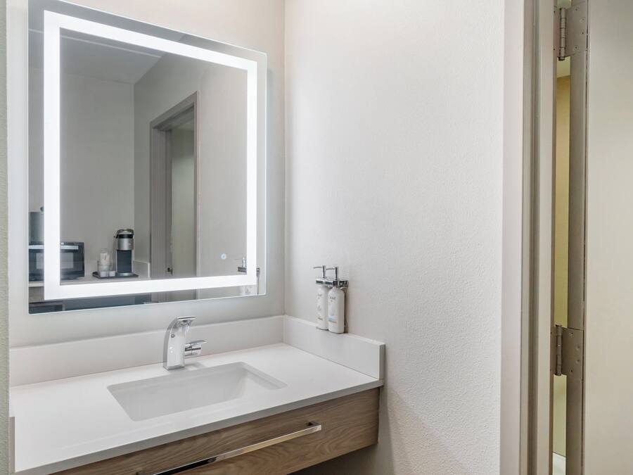 A bathroom with a white sink, a mirror, and a towel dispenser.
