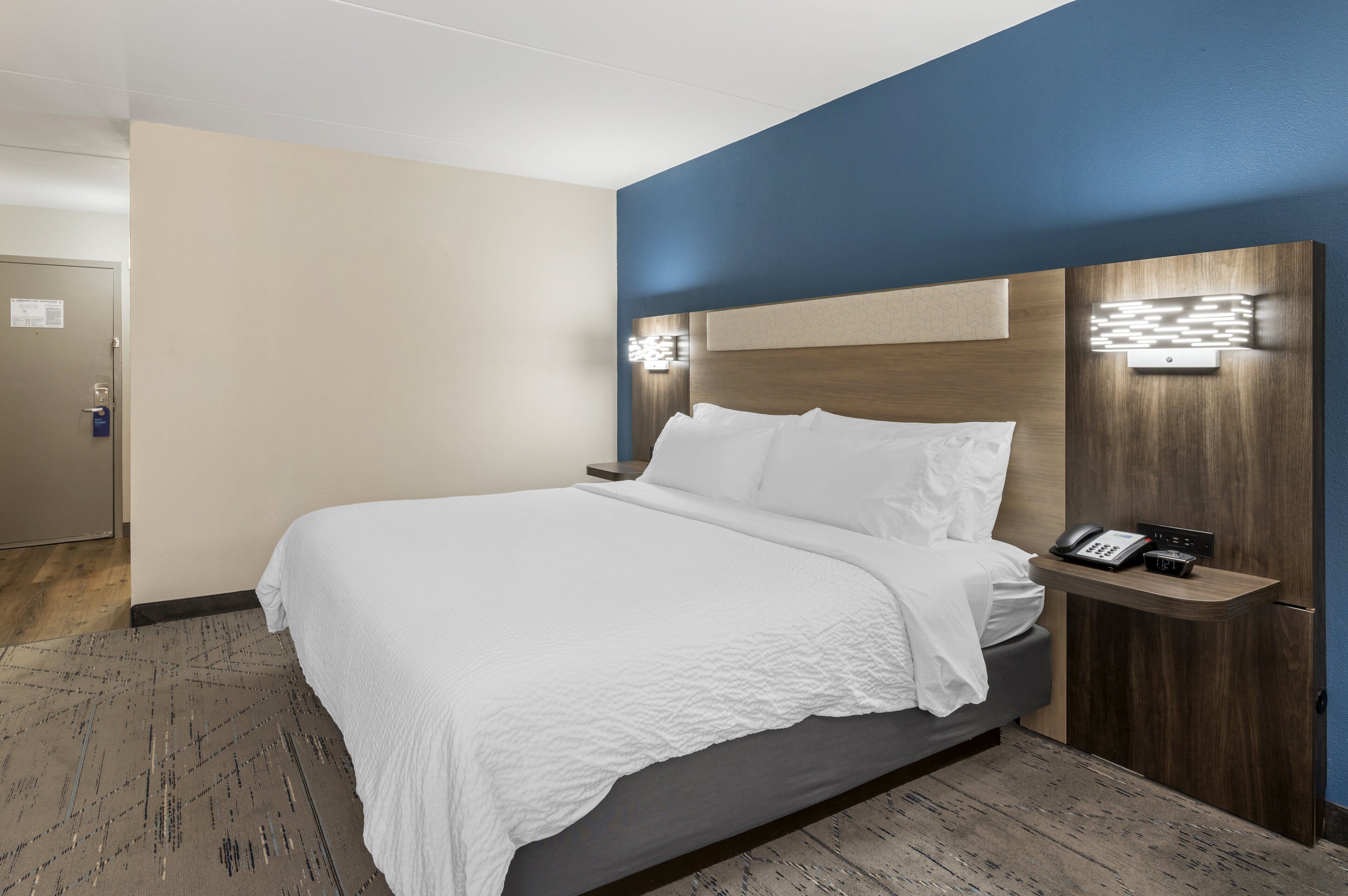 A hotel room with a bed, bedside table, and a wall-mounted light fixture.