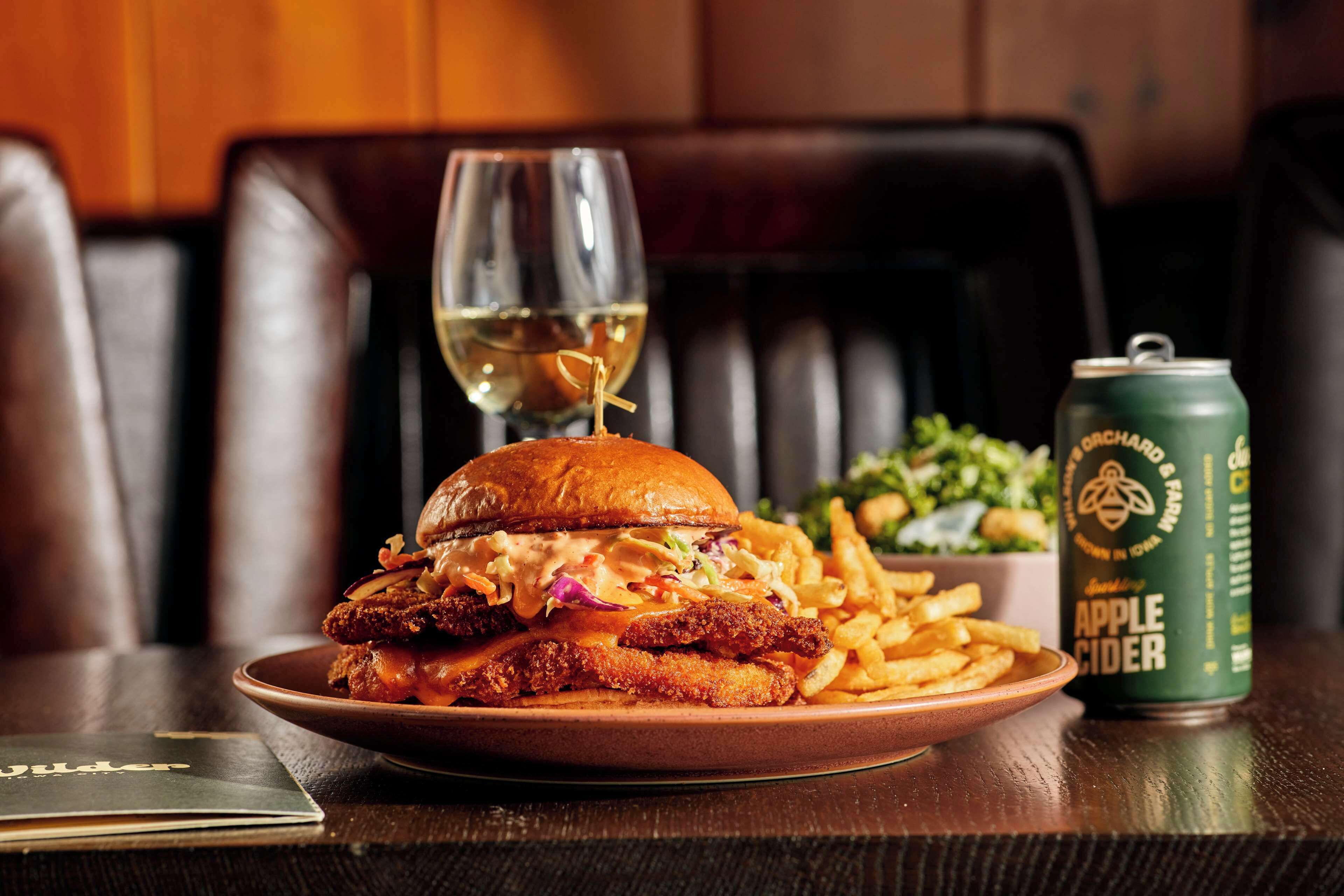 A plate with a sandwich, fries, and a can of apple cider on a table.