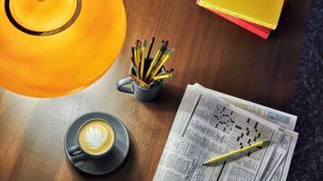 A table with a coffee cup, a teapot, a mug with pencils, and a newspaper.