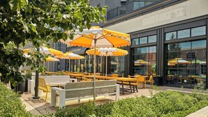 An outdoor seating area with yellow and white umbrellas, benches, and tables. - Graduate by Hilton Iowa City (Iowa City)