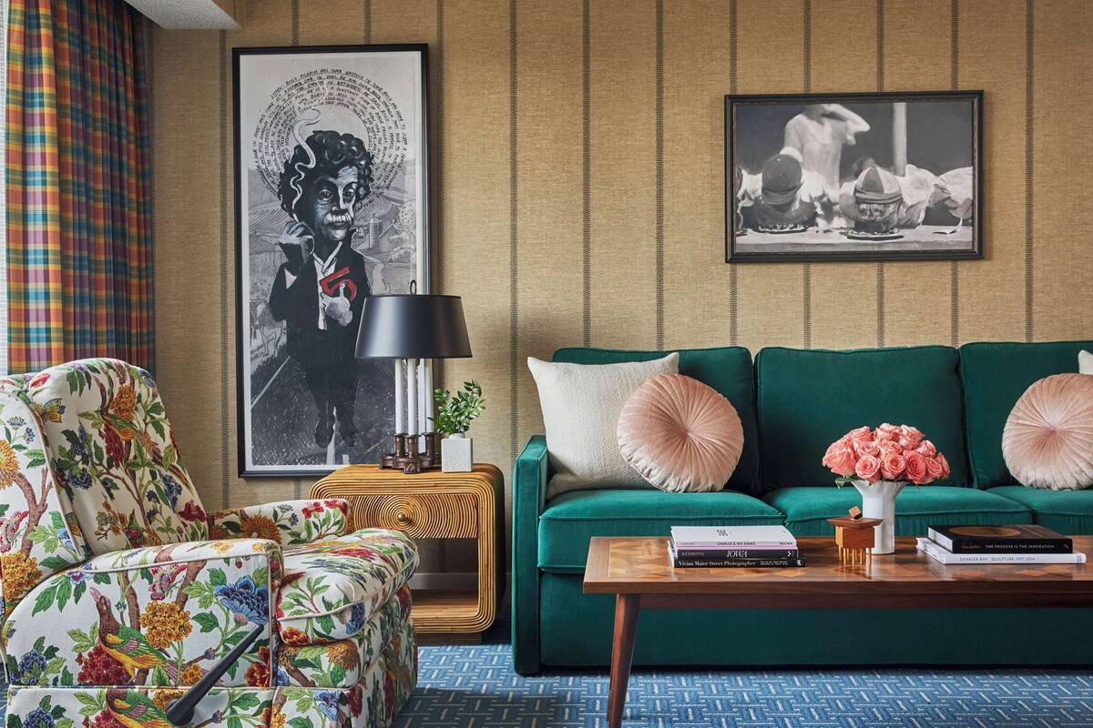 A living room with a green sofa, floral armchair, and a coffee table with books and a vase of flowers.