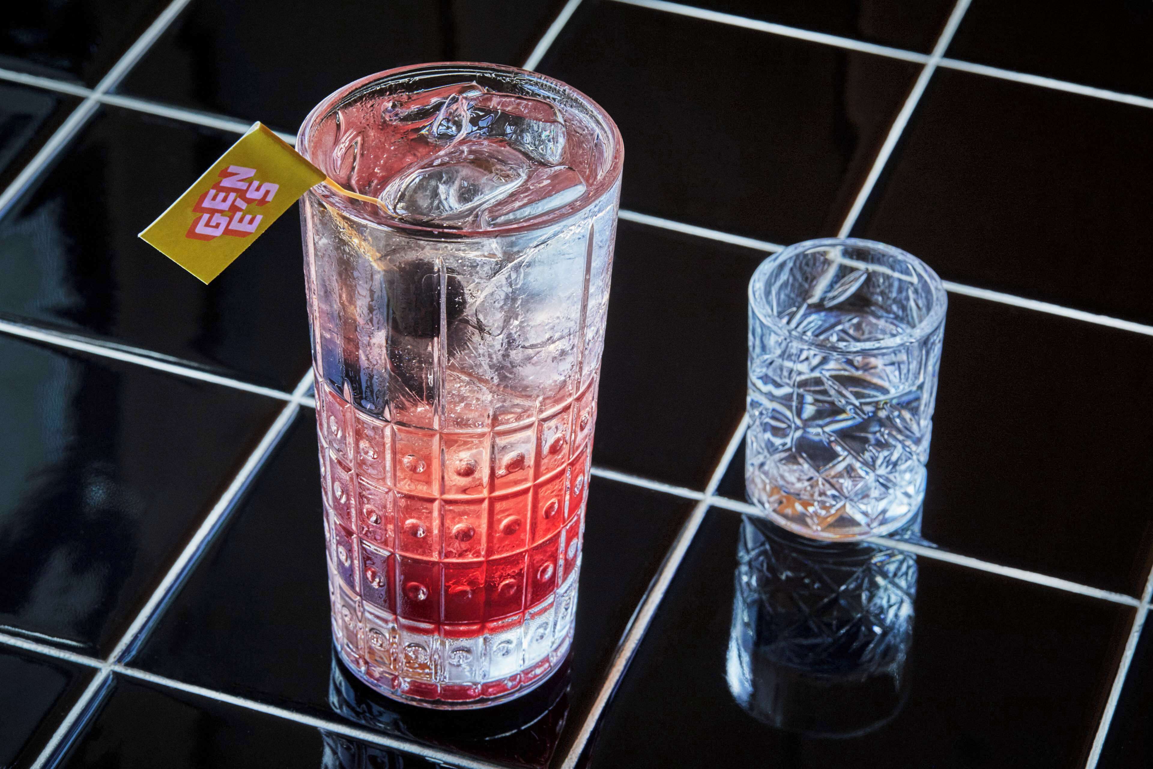 Two glasses of red beverage on a reflective black surface with a grid pattern.