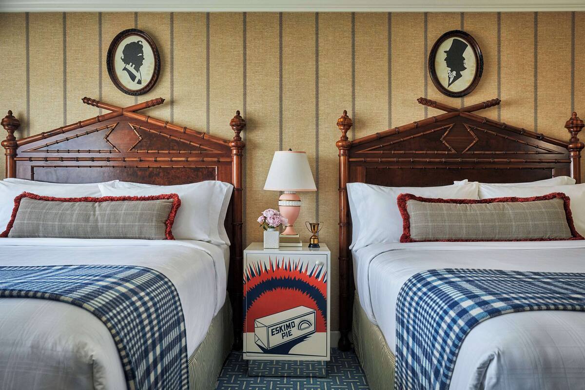 A hotel room with two wooden beds, a nightstand with a lamp, and a decorative box between the beds.