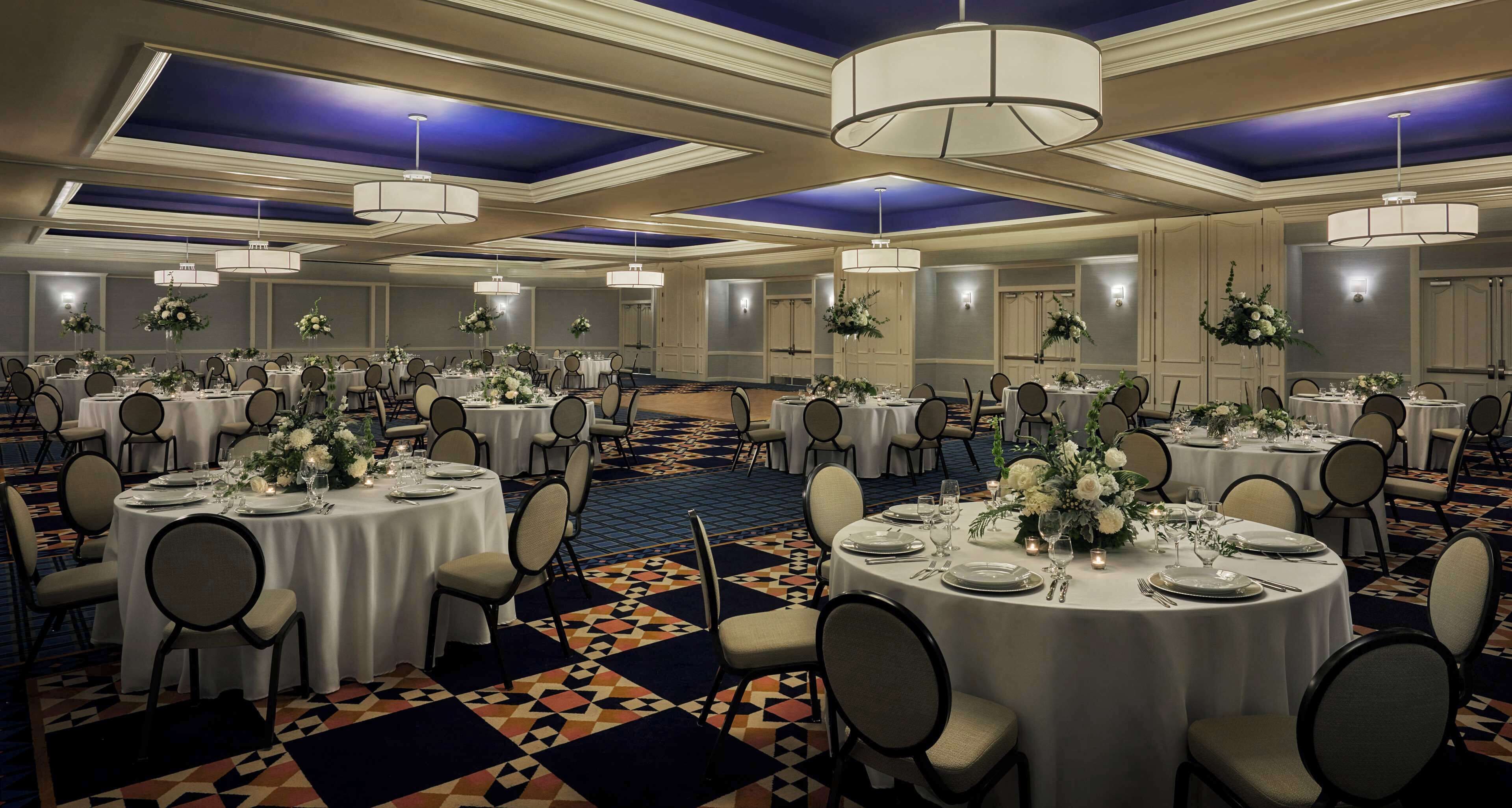 Un salón de banquetes con mesas redondas, sillas y centros de mesa florales.