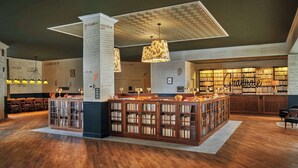 A library with wooden bookshelves, a central reading area with chairs, and a ceiling with a geometric pattern. - Graduate by Hilton Iowa City (Iowa City)