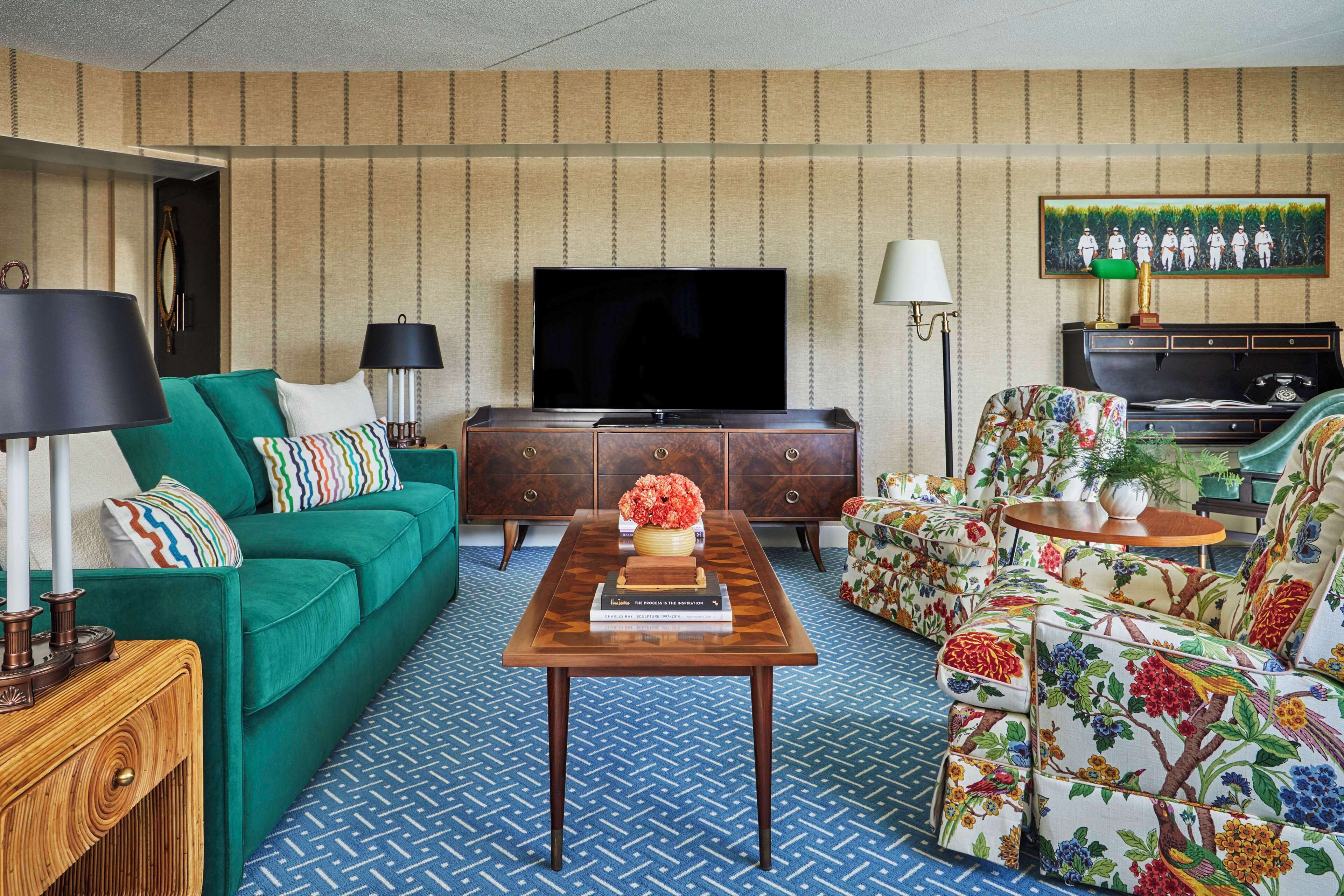 A living room with a green sofa, a wooden coffee table, a television, and a floral armchair.