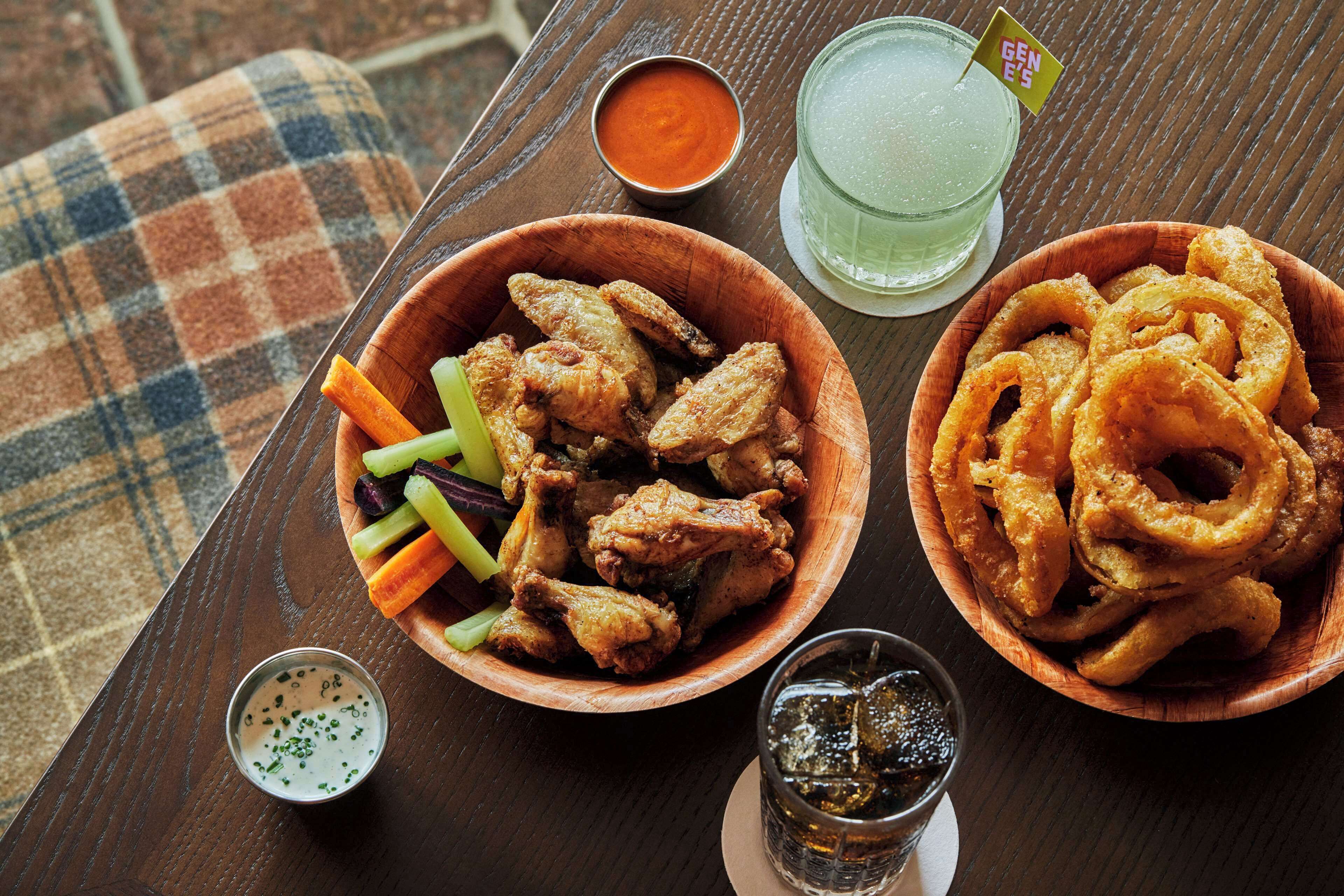Ett bord med en skål friterade kycklingvingar, en skål med lökringar och ett glas iste.