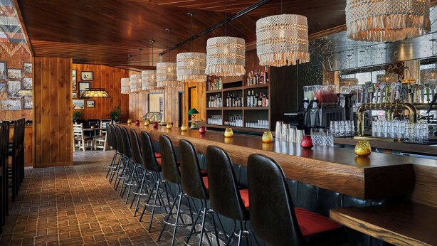 A bar area with wooden bar counters, black bar stools, and hanging woven light fixtures. - Graduate by Hilton Iowa City (Iowa City)