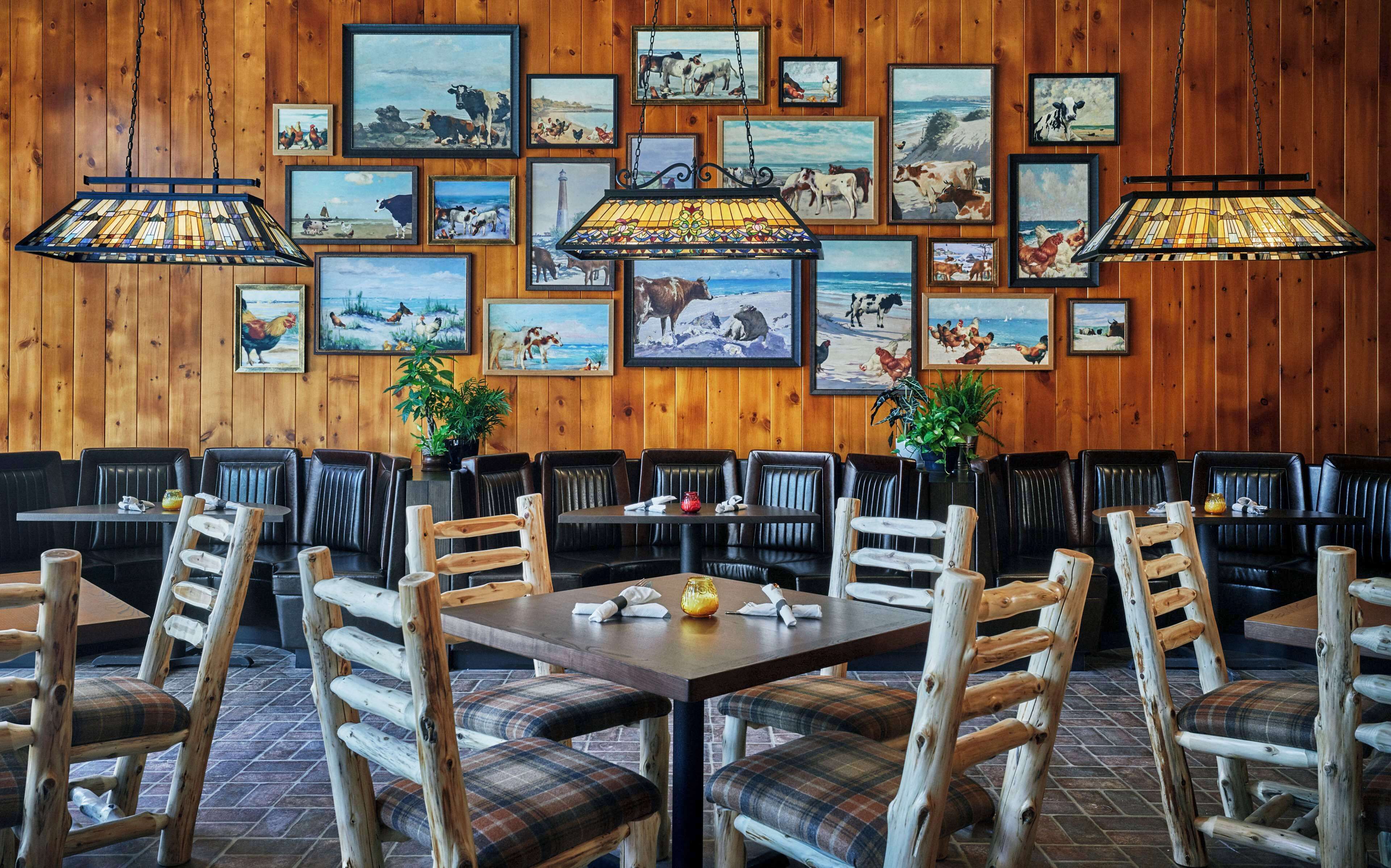 A restaurant with wooden walls, multiple framed paintings, and a mix of wooden and upholstered seating.