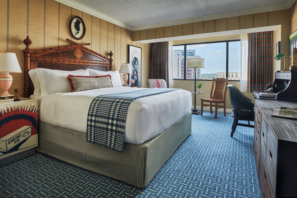 A hotel room with a large bed, a desk, a chair, and a view of the city.