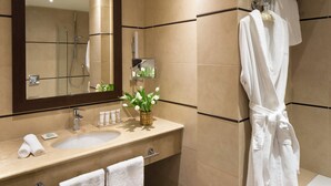 A modern bathroom with a large mirror, two sinks, a towel rack, and a shower area.