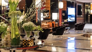 A modern lobby with a central table displaying floral arrangements, a hanging light fixture, and a television in the background. - Starhotels Ritz (Milan)