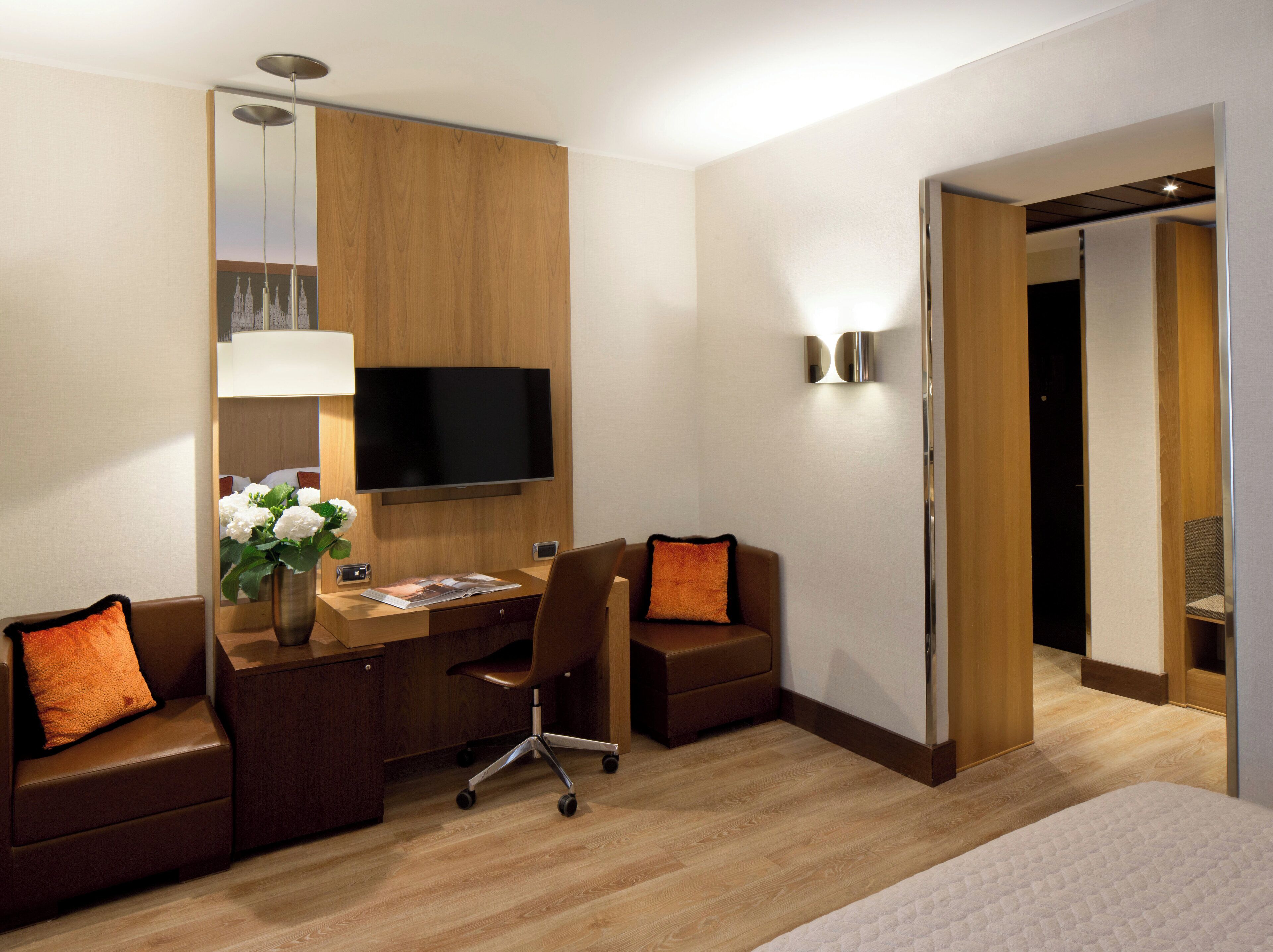 A hotel room with a wooden desk, a television, a chair, and a sofa.