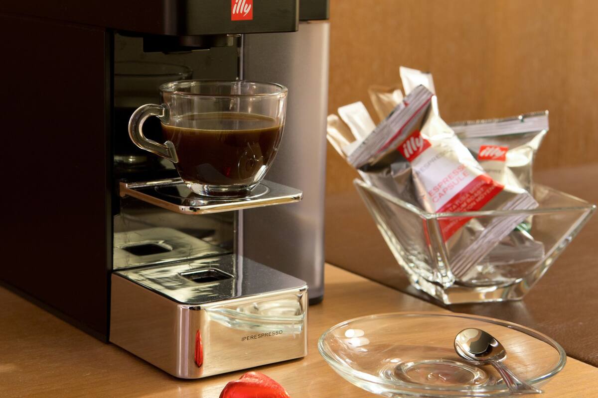 A coffee machine with a cup of coffee, a glass container with packets, and a spoon on a wooden table.